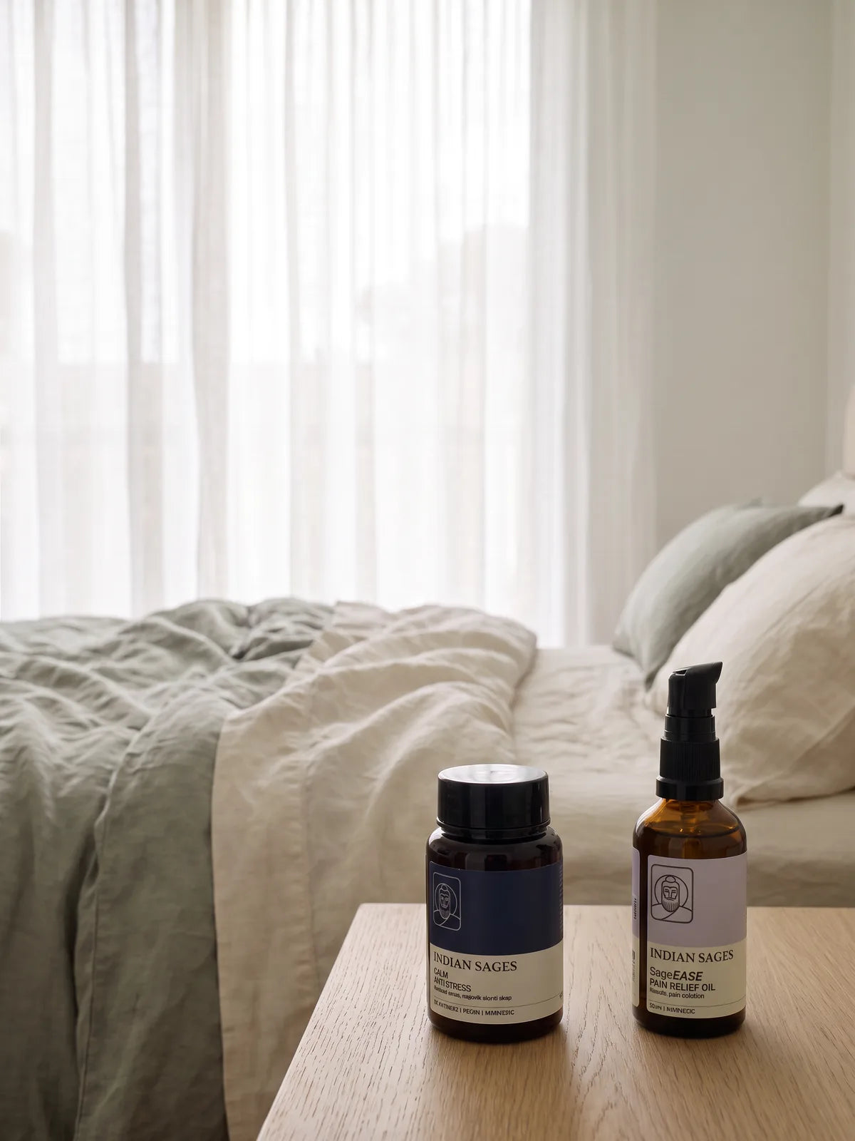 CALM capsules and SageEASE oil on a pale oak bedside table in soft morning light, beside a cup of chai.